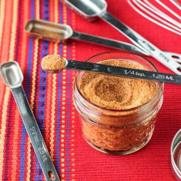 A glass jar of buffalo seasoning with various measuring spoons.