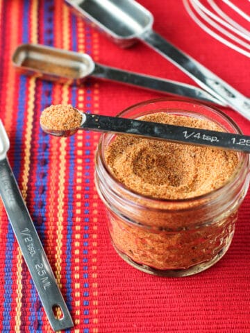 A glass jar of buffalo seasoning with various measuring spoons.