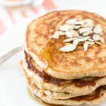 A stack of pancakes on a plate drizzled with maple syrup.