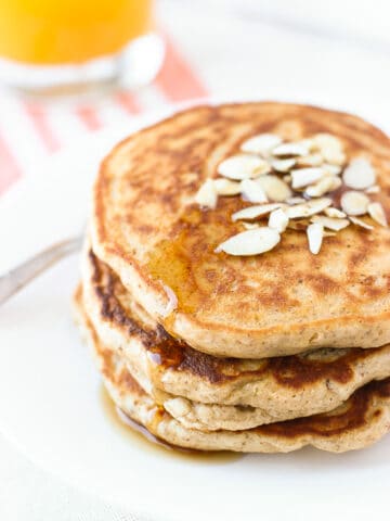 A stack of pancakes on a plate drizzled with maple syrup.