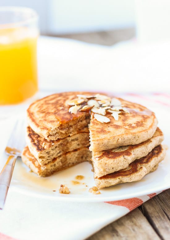 A profile-view of three pancakes on a plate with sliced almonds and syrup.