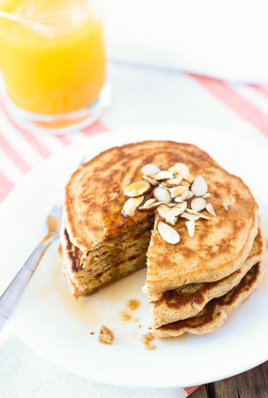 A stack of pancakes on a plate with a wedge taken out.