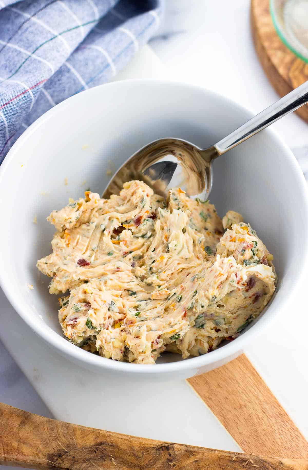 Softened butter combined with the rest of the ingredients in a ceramic bowl with a spoon