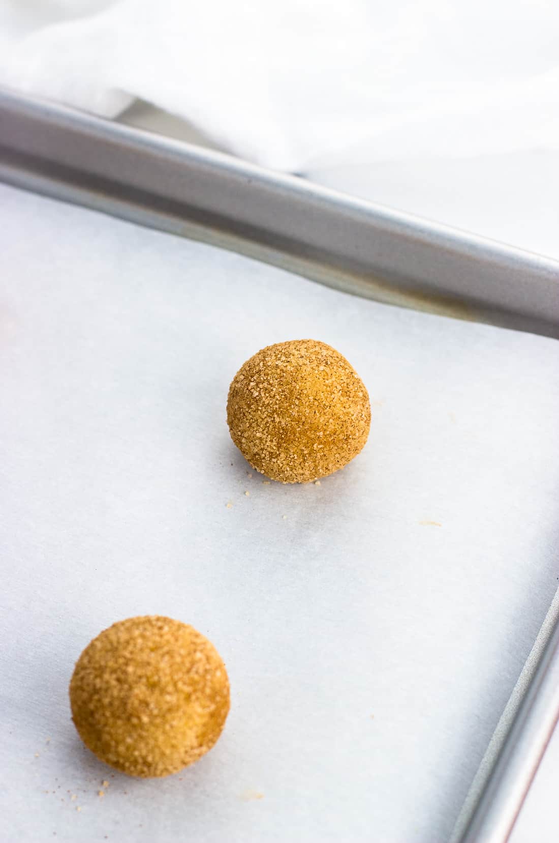 A ball of snickerdoodle dough rolled in cinnamon sugar and placed on a parchment-lined baking sheet, pre-bake