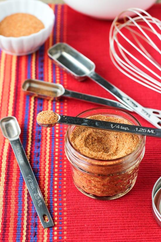 A small glass jar of buffalo spice blend with various measuring spoons.