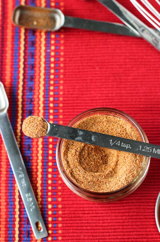 A close up of the metal quarter-teaspoon measuring spoon filled with mix resting on top of the glass jar of seasoning