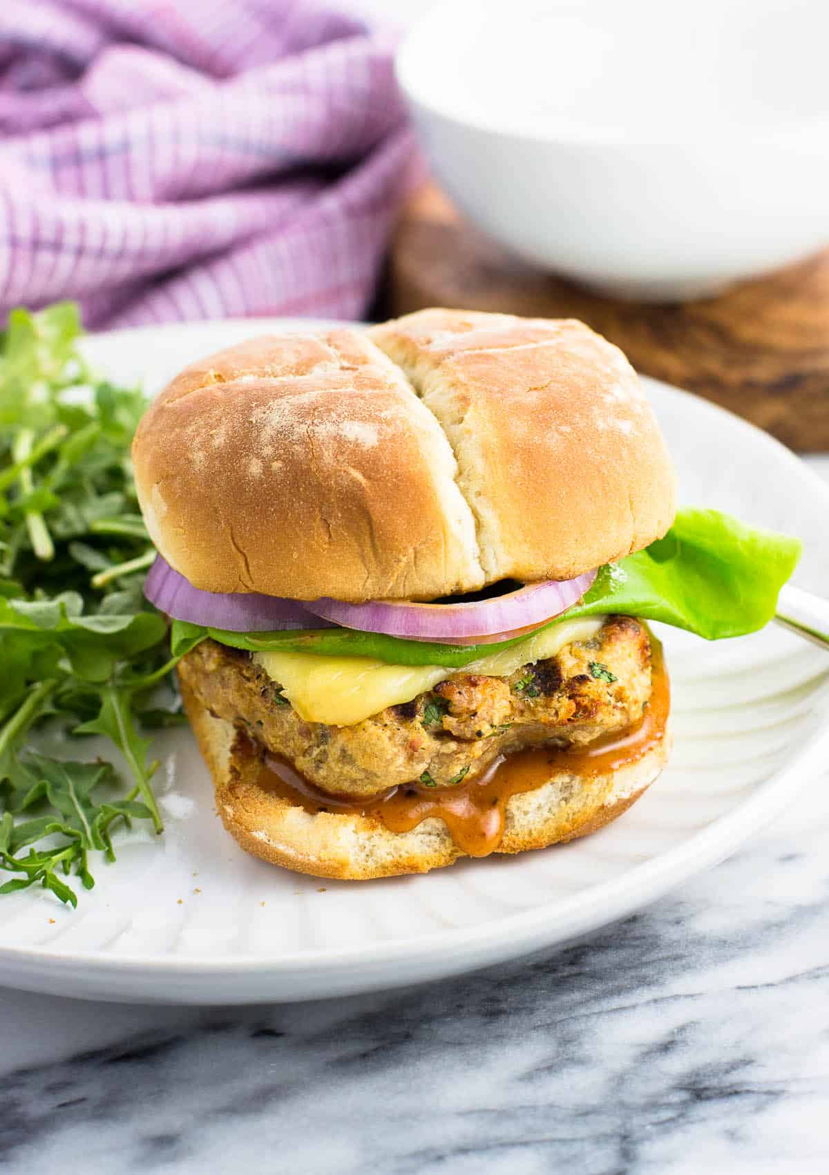 A chicken burger on a bun with toppings on a plate with salad.