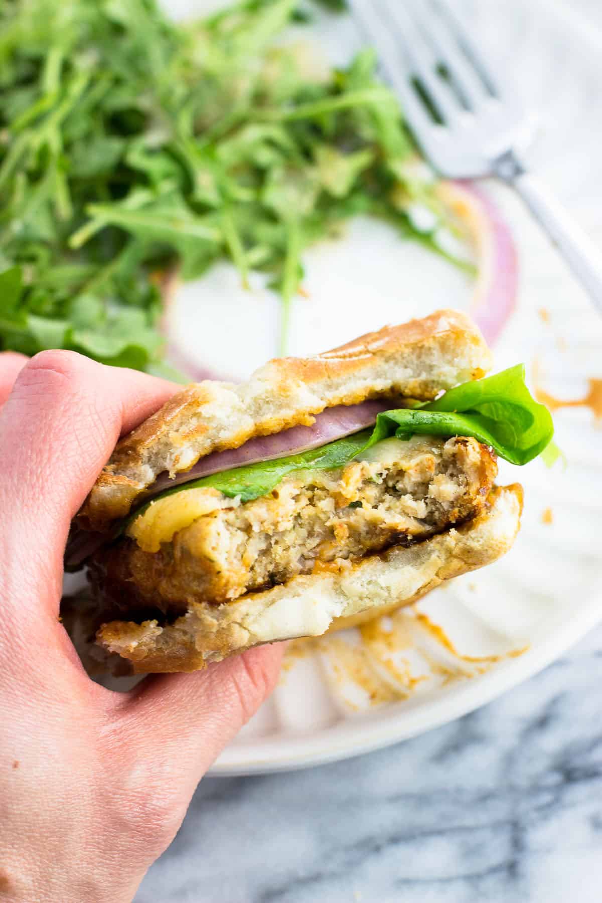 A hand holding a chicken burger with a bite taken out of it.