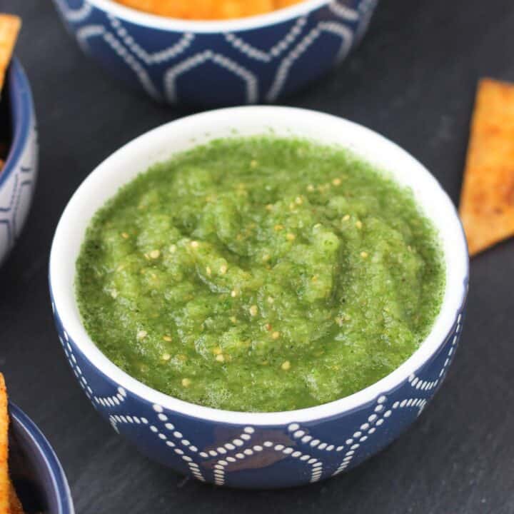A bowl of salsa verde with bowls of tortilla chips.