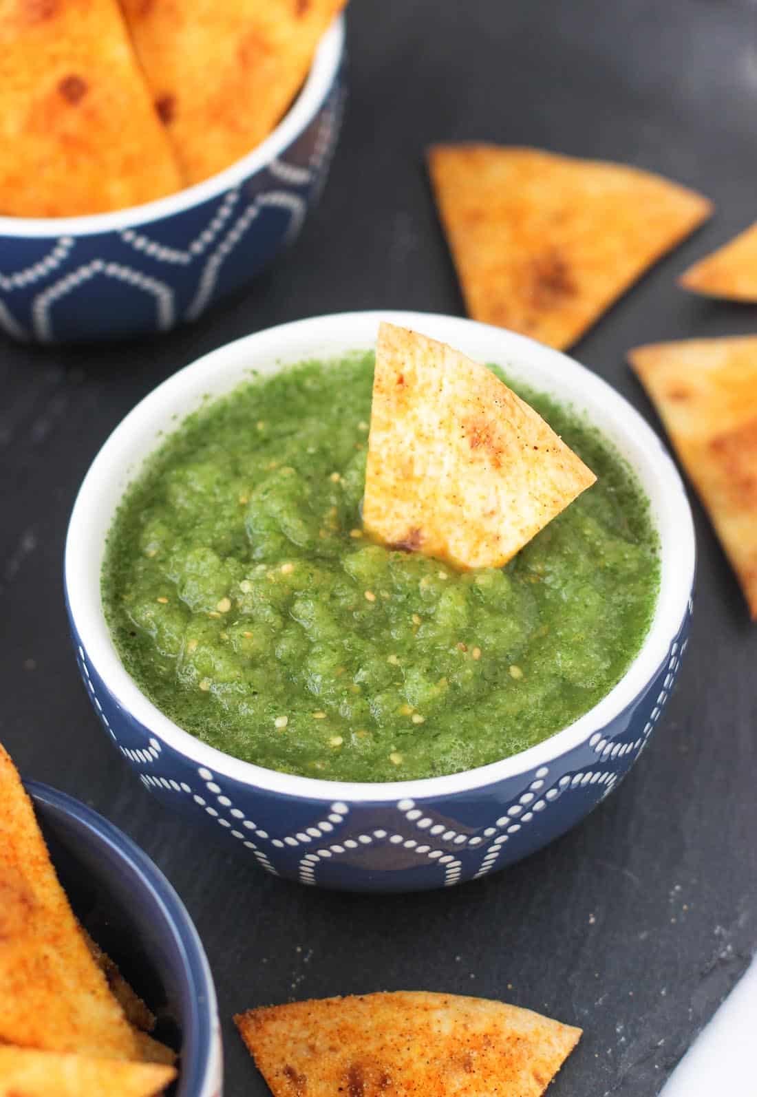 A tortilla chip dunked in a bowl of salsa verde.