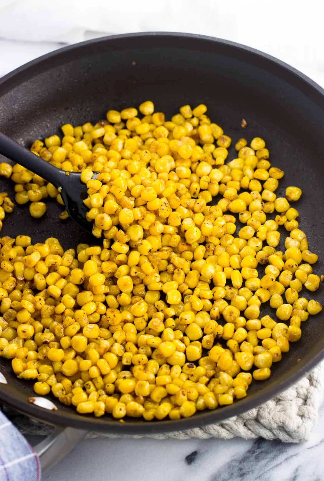 Roasted corn kernels in a skillet with a spatula.