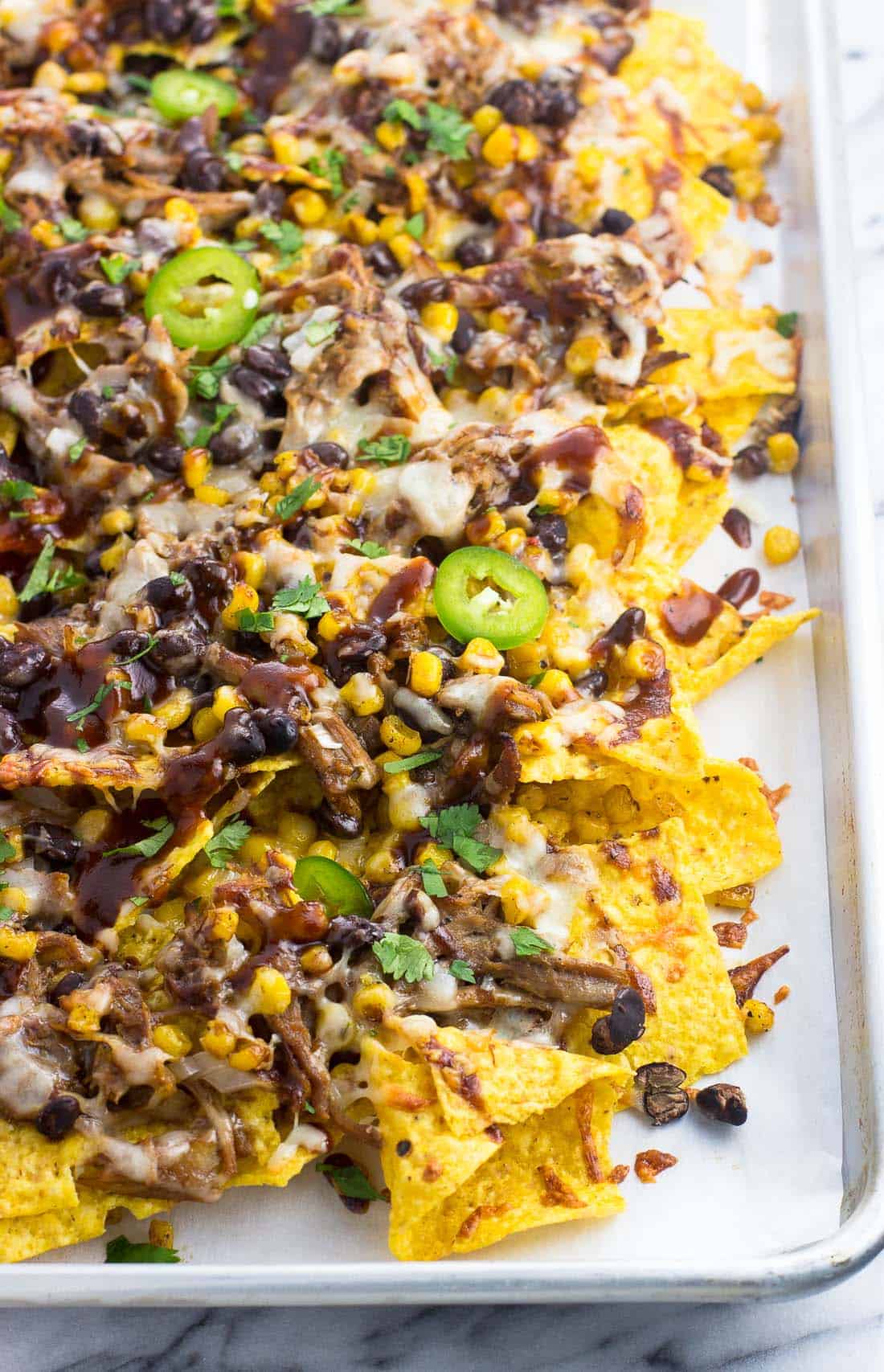 Baked BBQ pulled pork nachos on a tray topped with jalapeno slices.