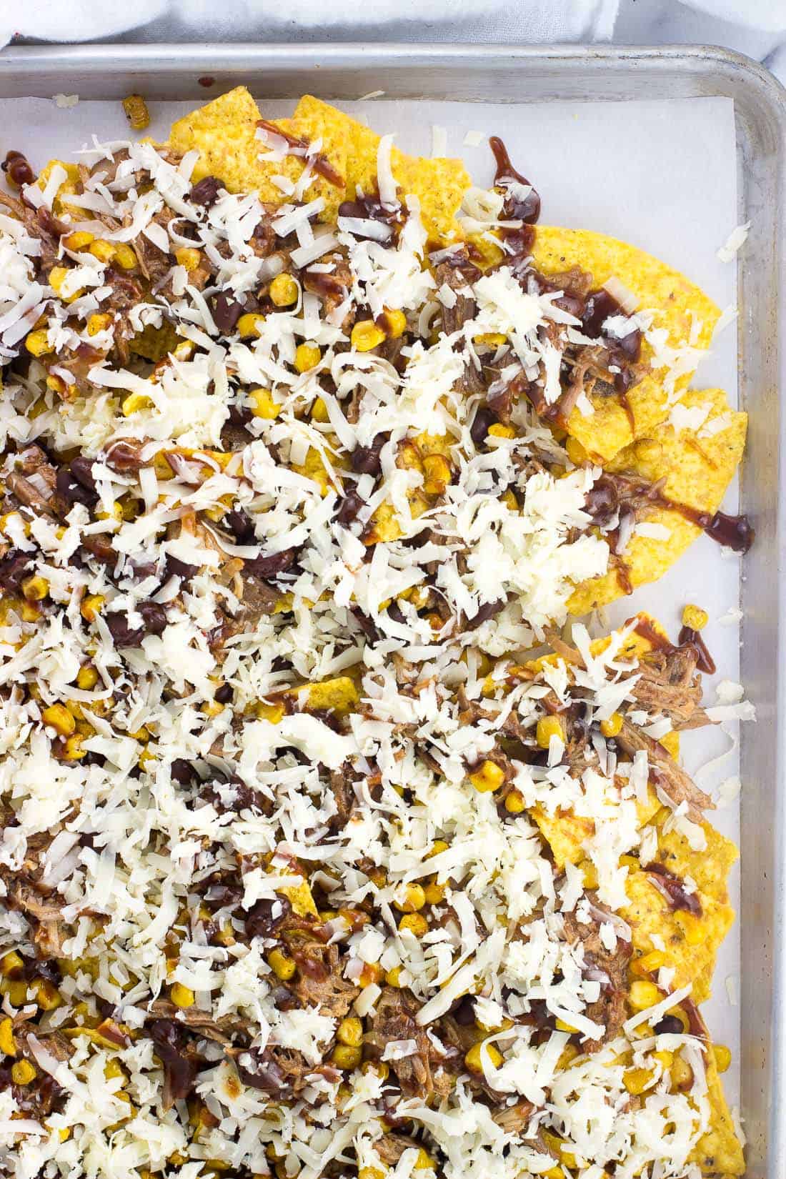 Tortilla chips, pulled pork, corn, and black beans on a sheet pan topped with shredded cheese before going in the oven.