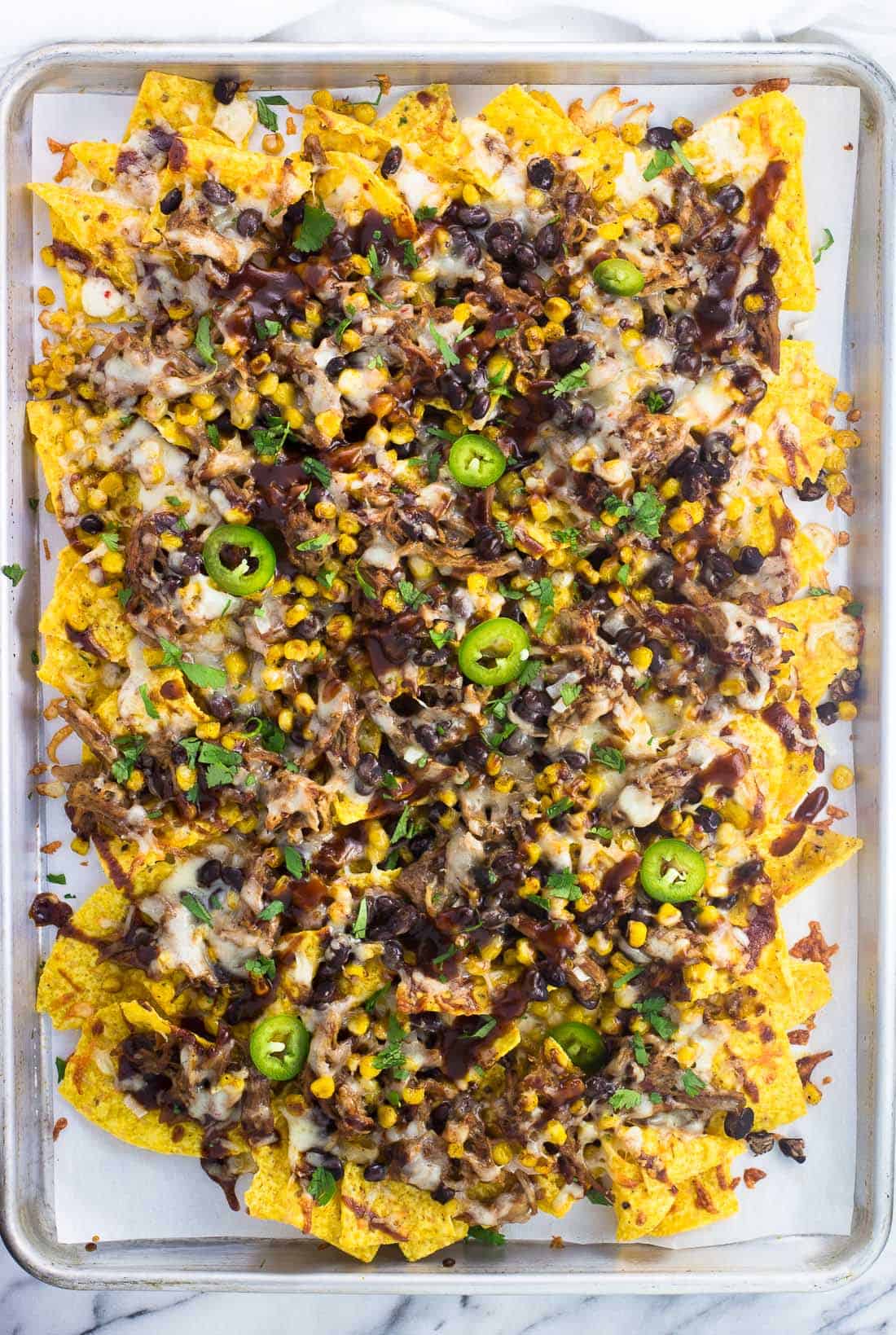 A sheet pan full of pulled pork nachos ready to serve.