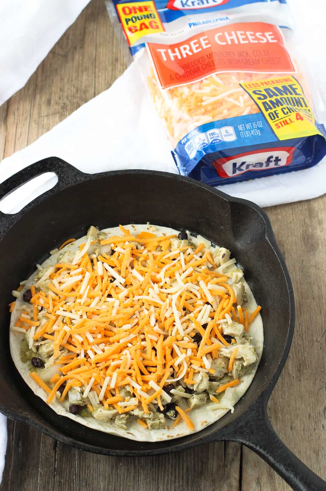 Tortilla pie mid-assembly next to the bag of shredded cheese.