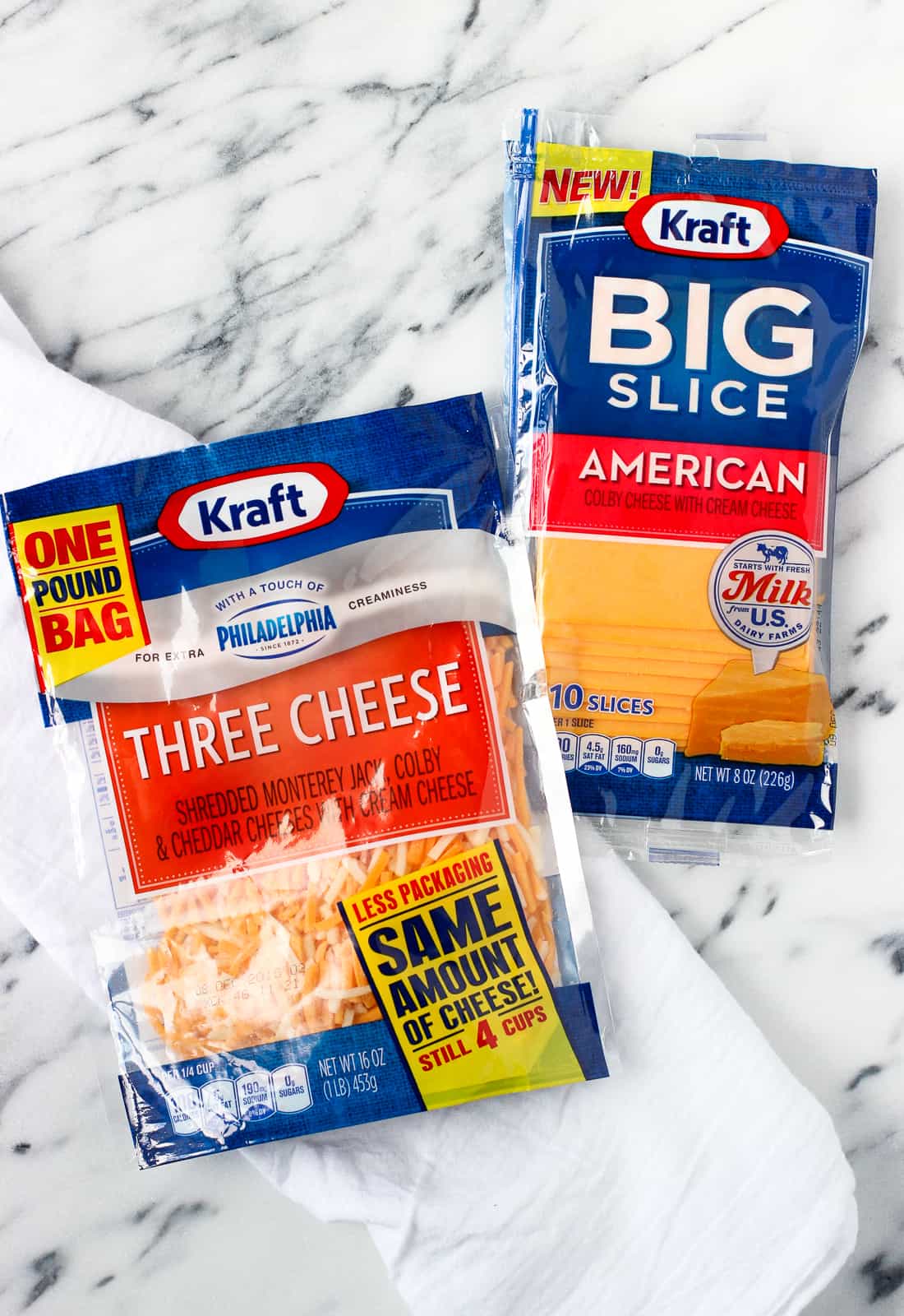 Two cheese packages, one shredded and one sliced, on a marble board.