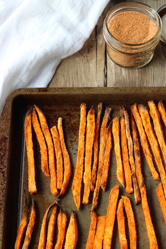 Lined up seasoned sweet potato fries on a baking sheet.