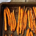 Baked sweet potato fries lined up on a metal sheet pan.