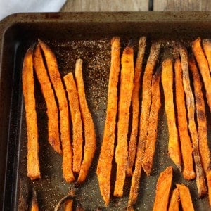 Baked sweet potato fries lined up on a metal sheet pan.