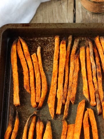 Baked sweet potato fries lined up on a metal sheet pan.