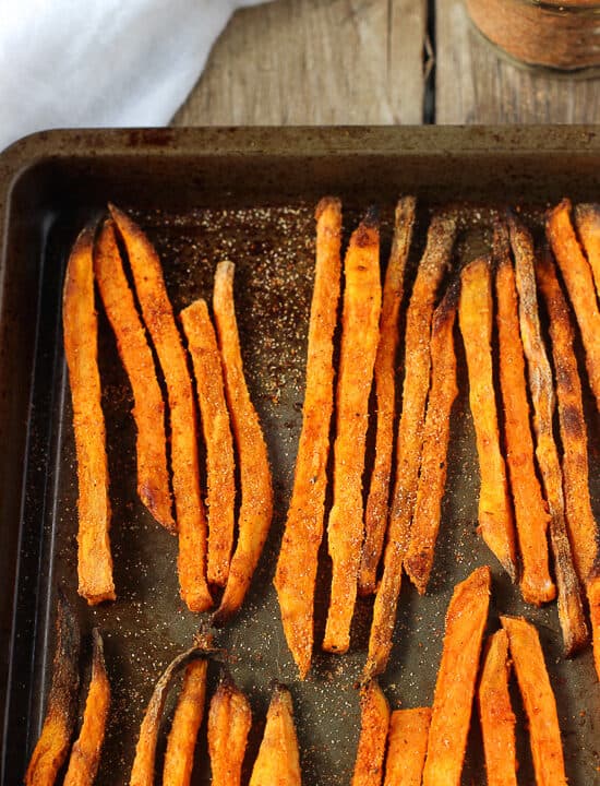 Baked sweet potato fries lined up on a metal sheet pan.