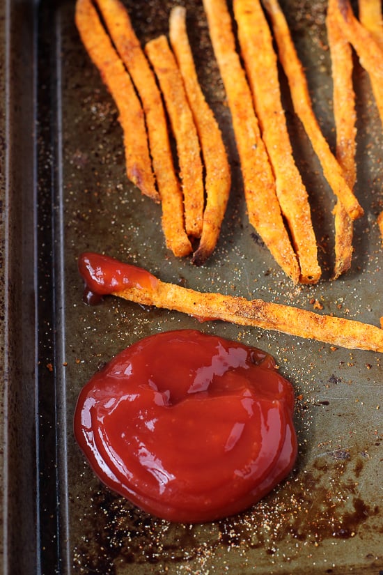Sweet potato fries on a metal baking sheet with a dollop of ketchup.