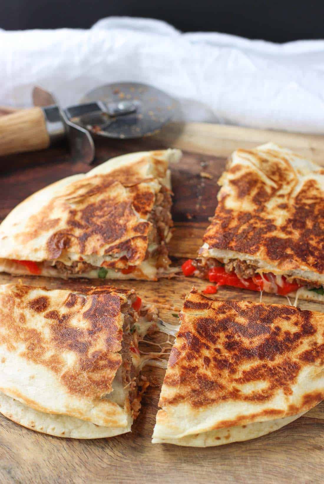 An Italian sausage quesadilla sliced on a cutting board.