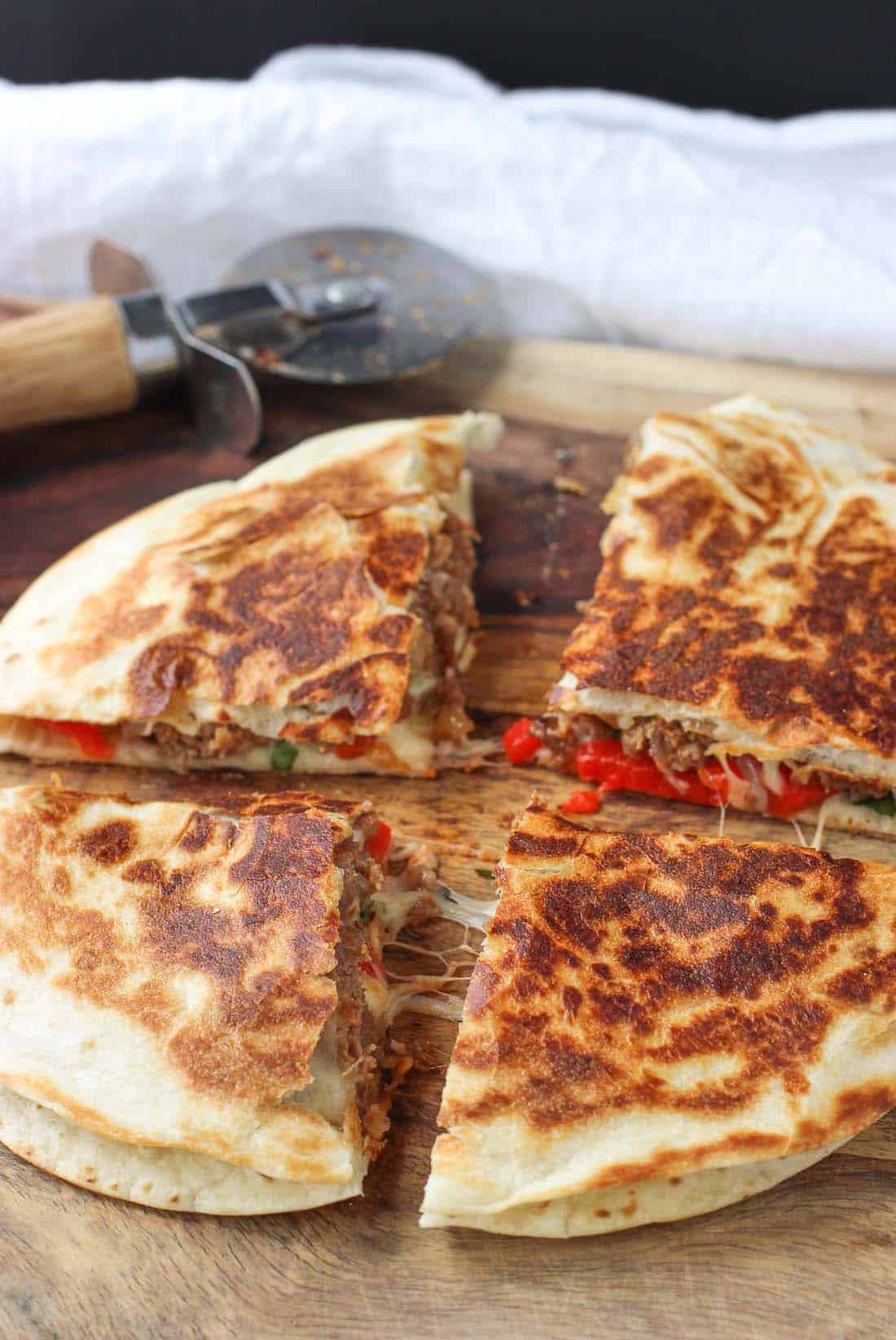 A quesadilla sliced into four equal pieces on a wooden cutting board.