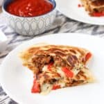 Stacked Italian sausage quesadillas on two plates with a dipping bowl of marinara sauce.