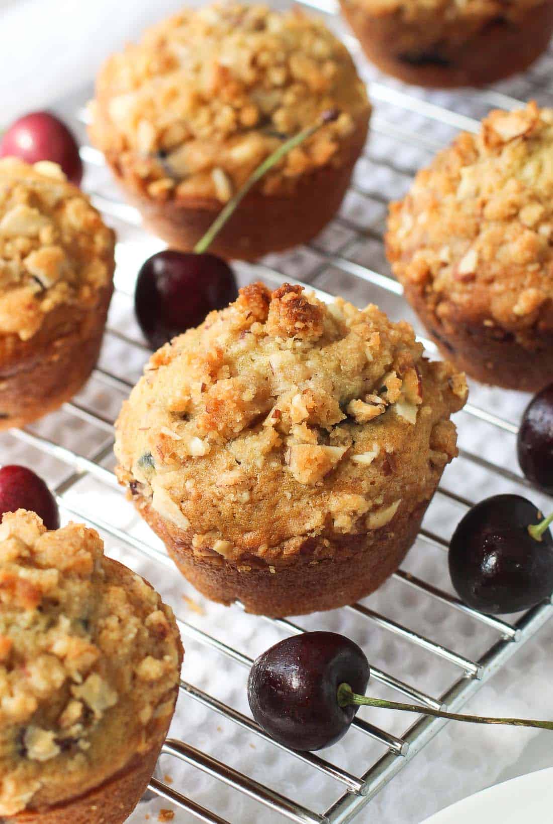Cherry almond muffins on a wire rack surrounded by fresh cherries