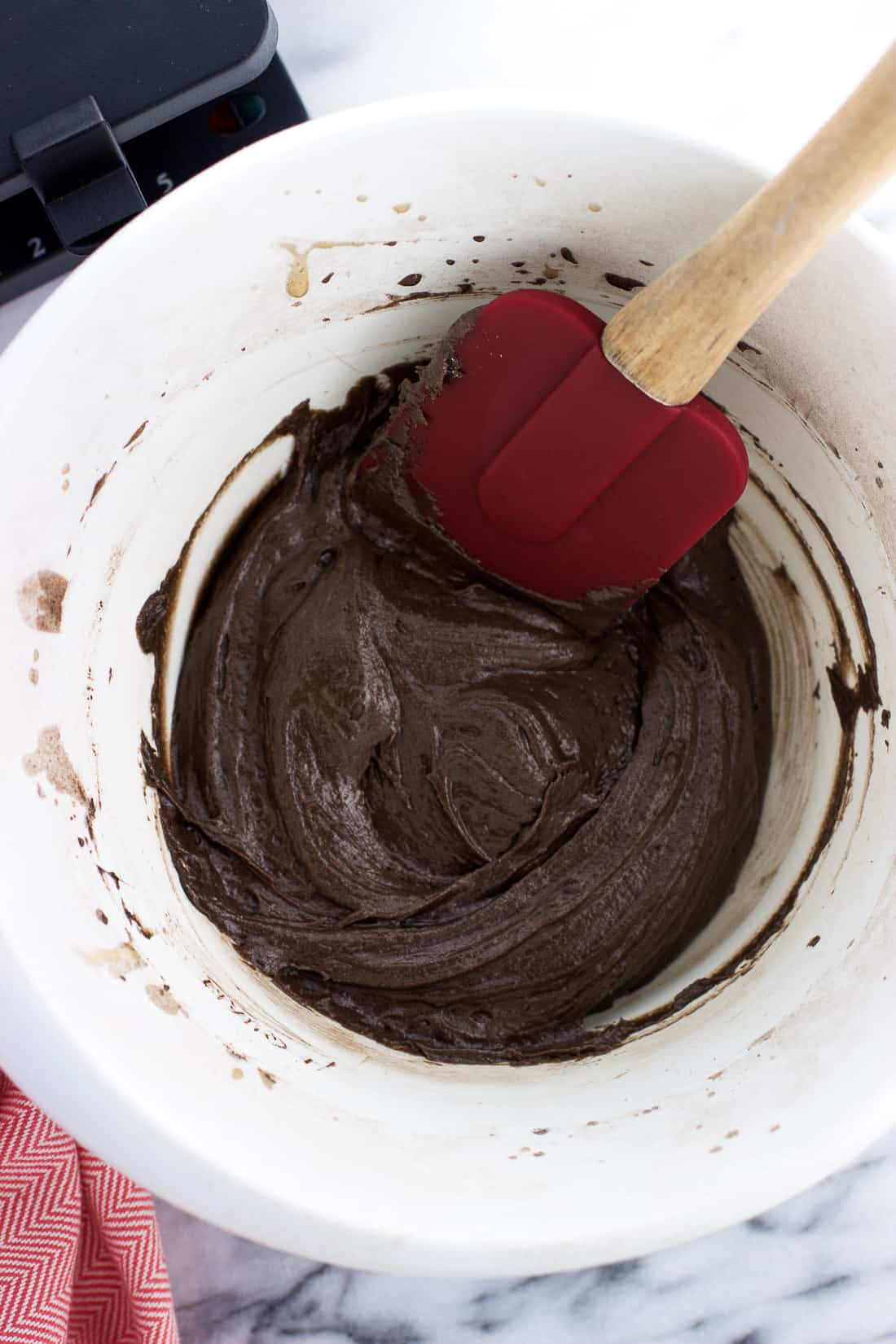 Chocolate pizzelle batter in a plastic mixing bowl with a spatula.