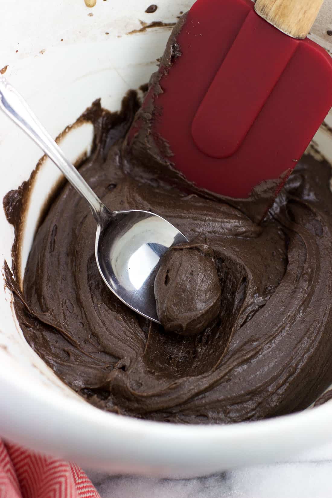 A spoon scooping a ball of cookie batter out of the mixing bowl.
