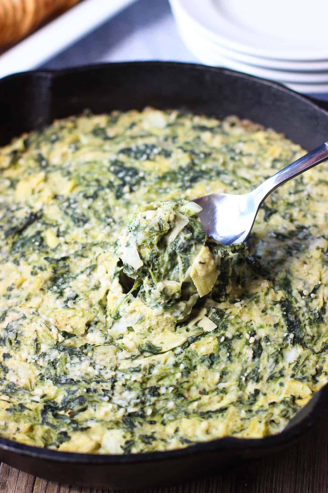 A spoon scooping spinach artichoke dip out of the pan.