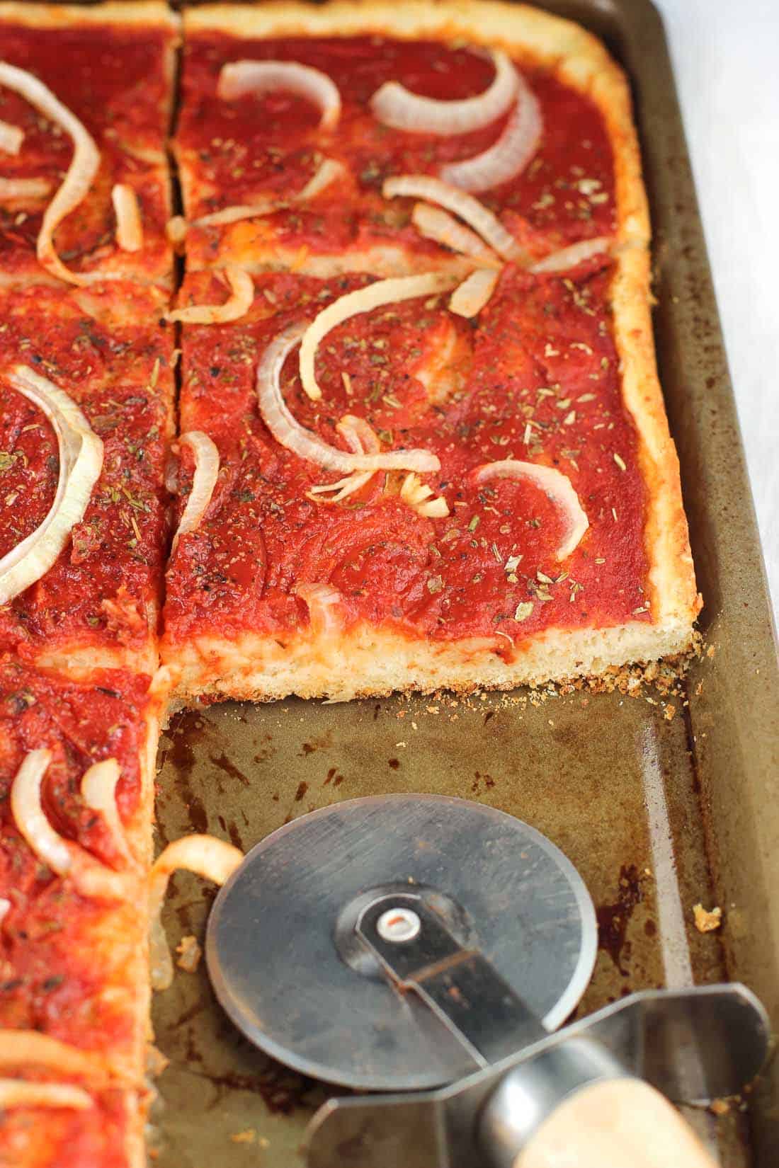 Sliced focaccia pizza on a sheet pan with a pizza cutter.