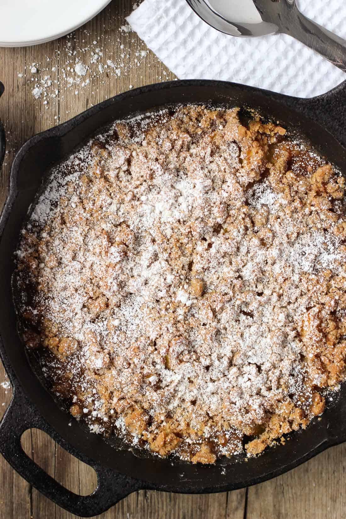 An overhead shot of a cast iron pan of peach crisp after cooling and dusting with confectioners' sugar