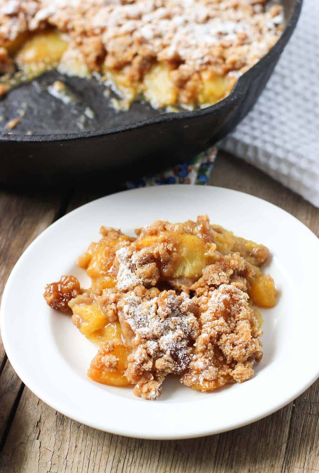 A portion of peach crumble on a small ceramic dessert plate with the whole pan in the background