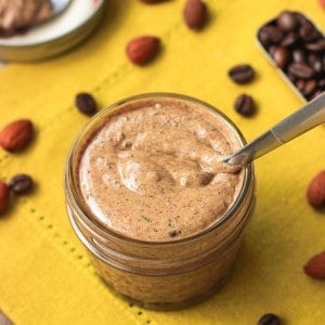 A spoon plunged in a small glass jar filled with almond butter