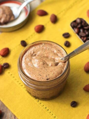 A spoon plunged in a small glass jar filled with almond butter