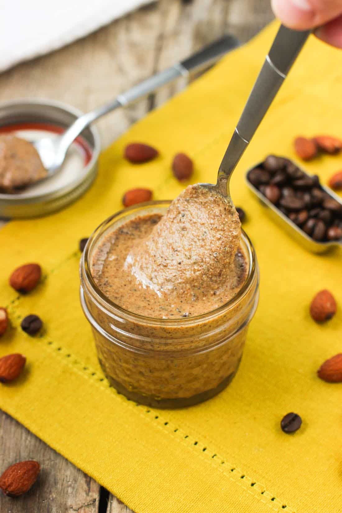A spoonful of almond butter being lifted out of the glass jar