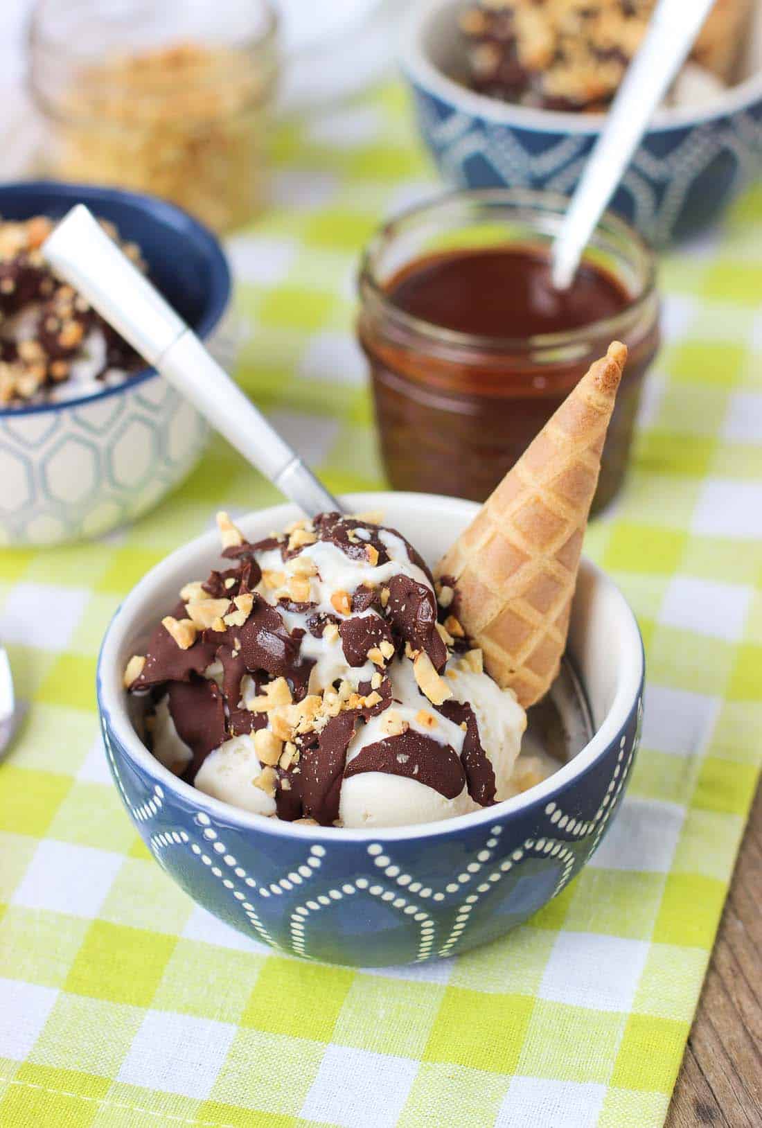 An ice cream sundae in a bowl with a spoon having cracked the hardened shell coating