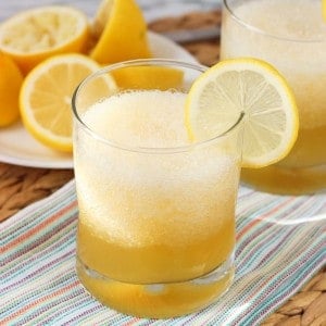 A gold rush cocktail with crushed ice in a short glass garnished with a lemon round with extra lemons in the background