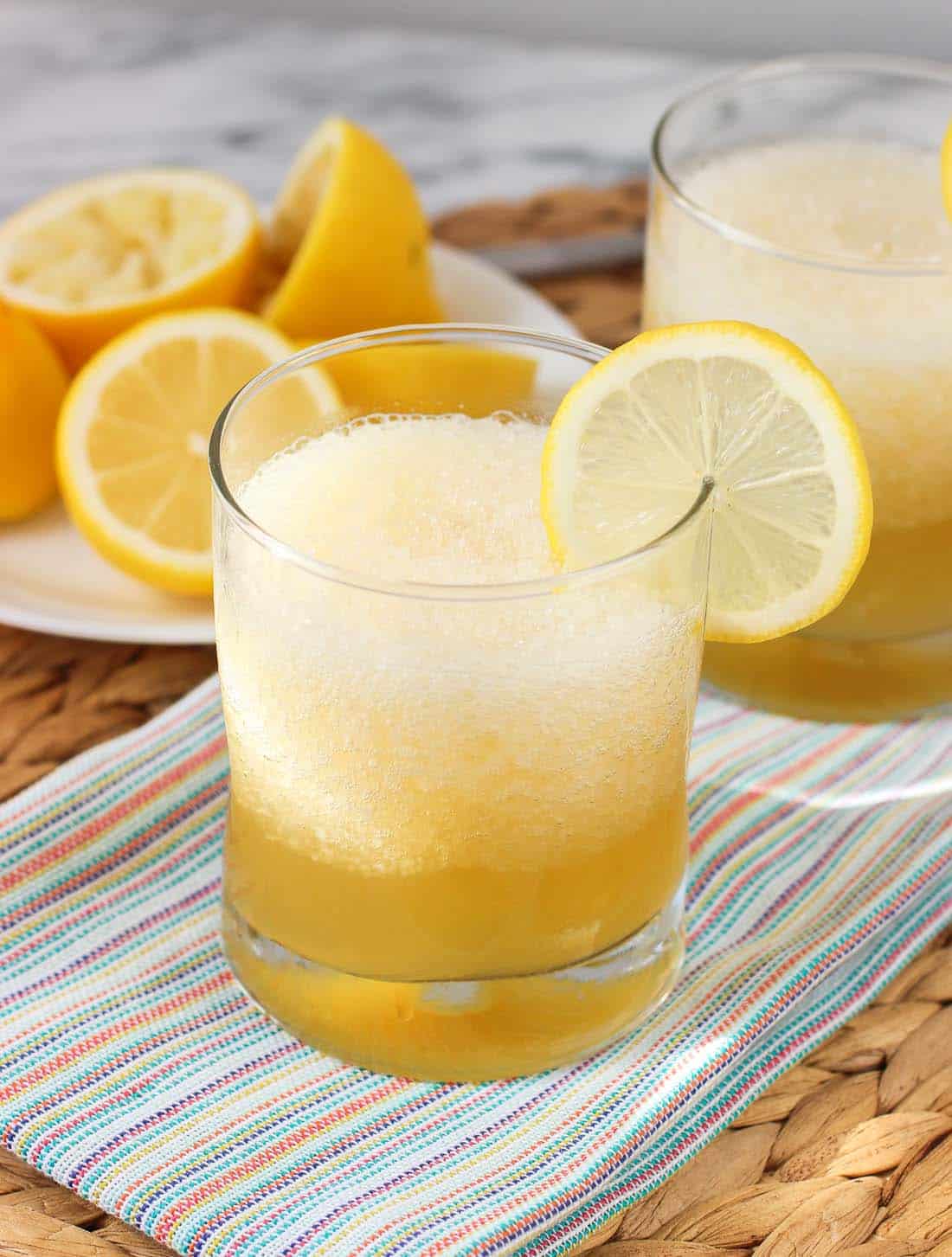 A gold rush cocktail with crushed ice in a short glass garnished with a lemon round with extra lemons in the background