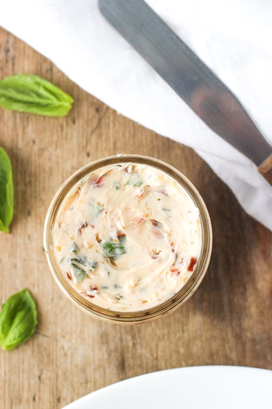 An overhead picture of a small glass jar of the softened compound butter next to fresh basil leaves