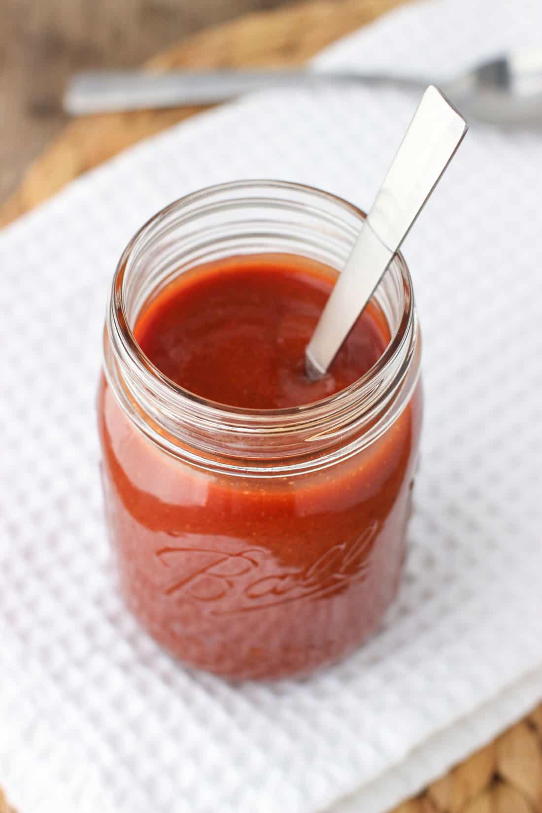 A spoon in a large glass jar of BBQ sauce.