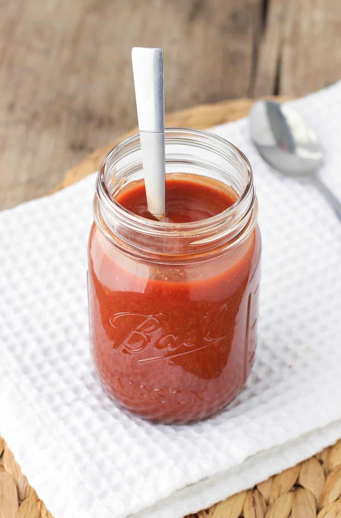 A spoon in a large glass jar of BBQ sauce.