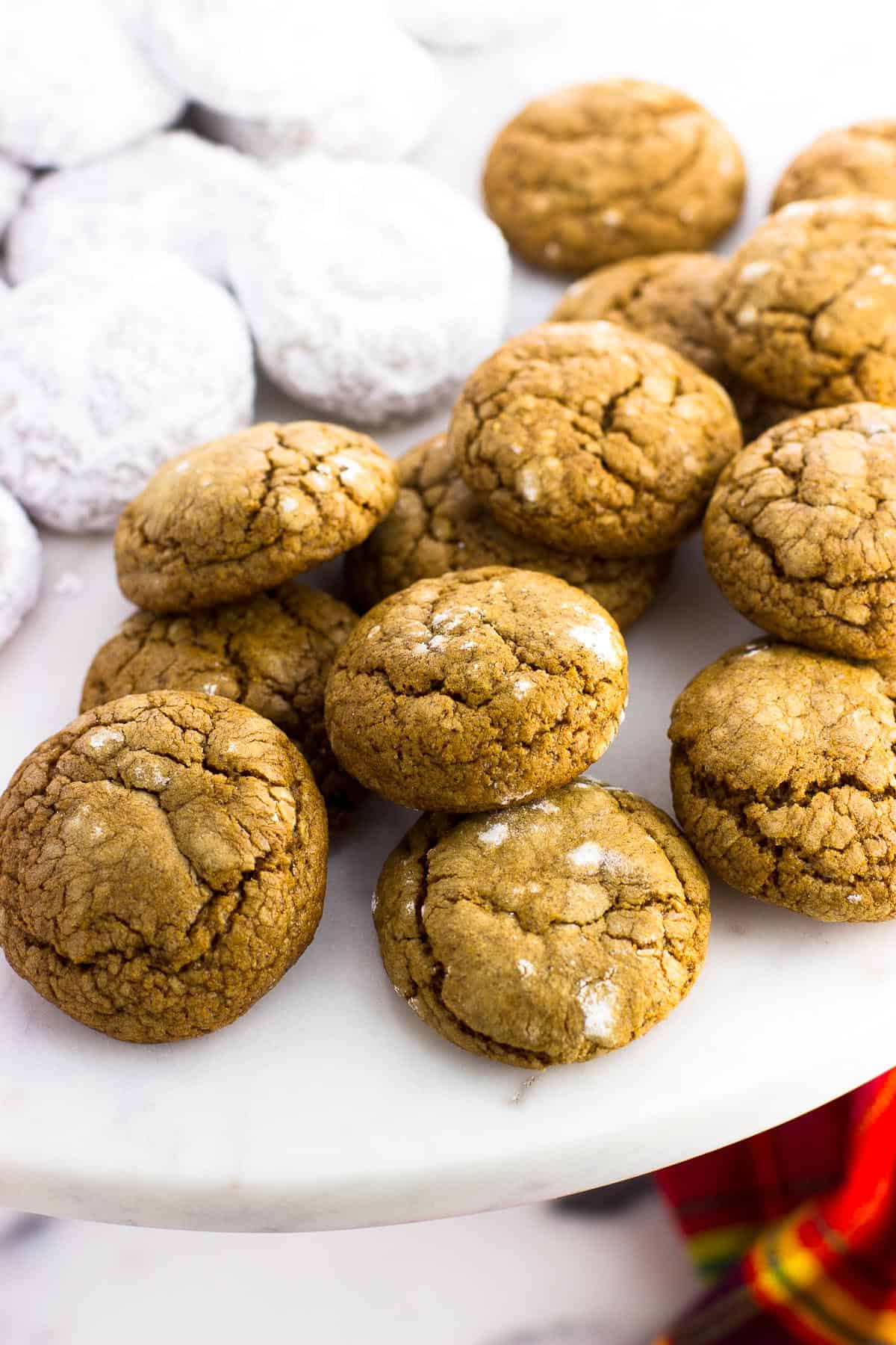 A platter of pfeffernusse cookies with one half as-is and the other half coated in powdered sugar