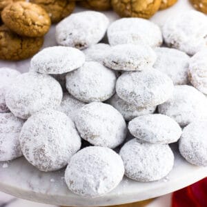 A pile of powdered sugar-coated pfeffernusse cookies on a marble cake stand.