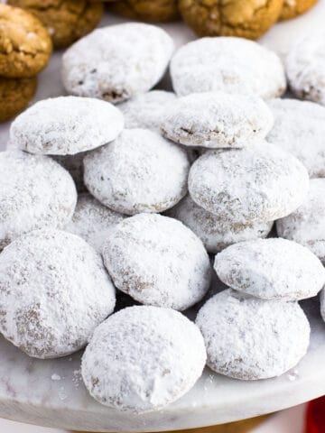 A pile of powdered sugar-coated pfeffernusse cookies on a marble cake stand.