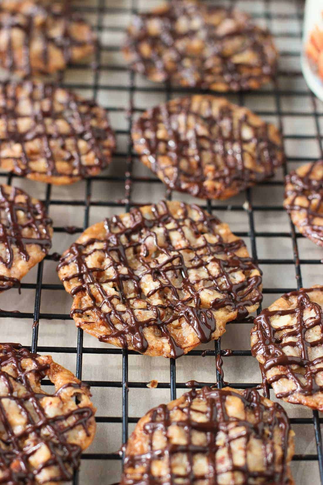 Melted chocolate drizzled on florentines on a wire rack.