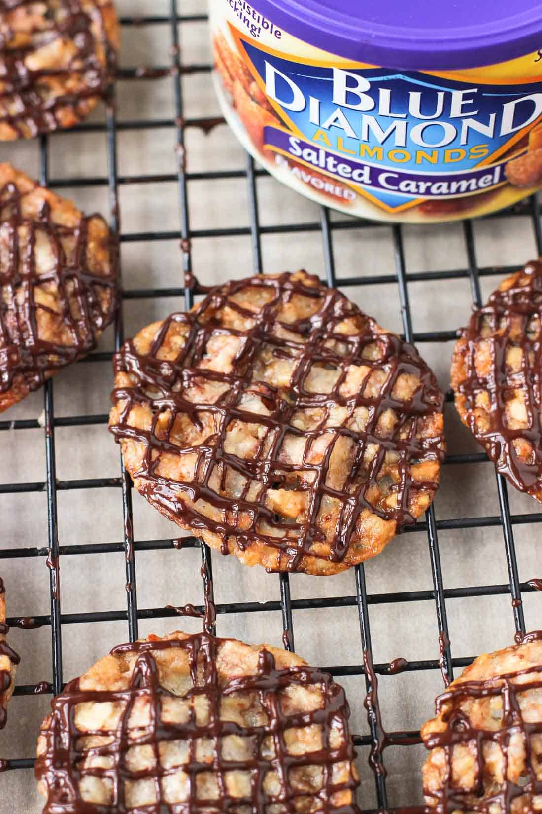Chocolate-drizzled florentines on a wire rack near the can of almonds.